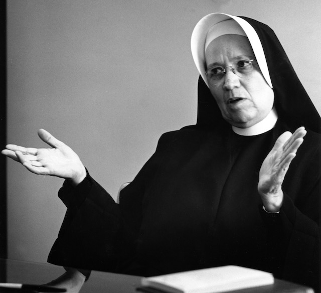 A black and white photo of a middle aged nun in a habit speaking using her hands.
