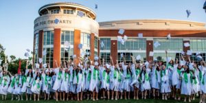 A large group of Nerinx Hall High School seniors in their white graduation caps and gowns throwing their caps in the air in celebration.