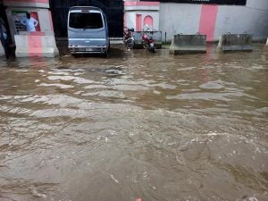 A flooded street and garage where the van tires are submerged in murky brown flowing water.