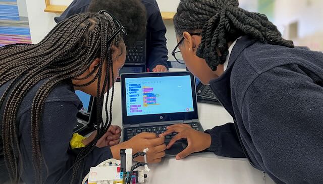 Two girls look intently at a computer screen as they are working on a robotics project.