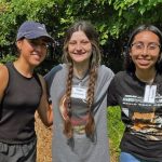 Three girls join together and smile for a picture as they take a break from spreading mulch.