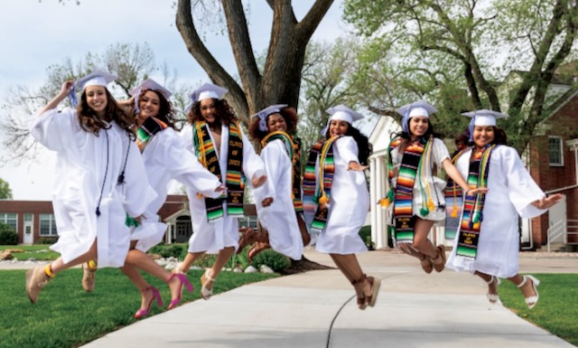 Seven graduated seniors from St. Mary's Academy jumping in their graduation caps and gowns outside of their school.