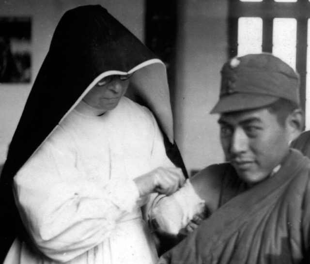 A black and white photo of a nun in a habit attending to a wounded soldier.