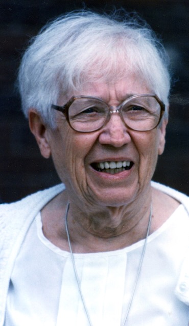 An older white woman with round glasses and white hair is caught in a candid shot half smiling and looking away from the camera.