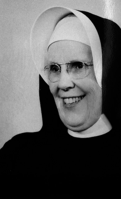 A black and white photo of an older nun wearing a traditional habit and glasses.