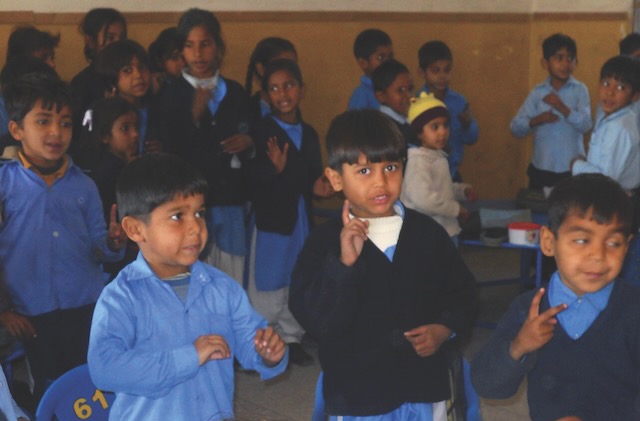 A classroom full of young students in Lahore, Pakistan engaged in a learning activity. Their uniforms are blue collard long sleeve shirts and some have black sweaters on top.