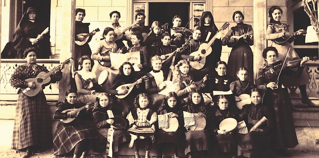 Sepia toned group photo of a 19th century music class where the entire class is holding instruments.