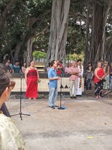 A man with a blue shirt talking into a microphone speaking to a crowd of people.
