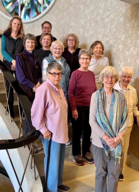 Eleven woman stand in staggered rows on a staircase smiling for a group photo