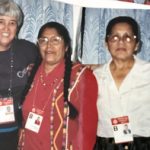 Five women smiling together for a group picture indoors, they are all wearing lanyard with large photo ID's.