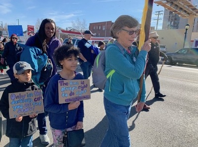 A march with a wide variety of attendees holding different signs on a sunny day.