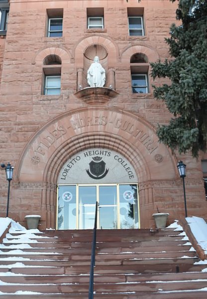 The front entrance of a large brick building with a large staircase sprinkled with snow before the front doors.