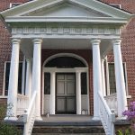 The front entrance of a red brick building with a large white awning with 4 columns creates a grand entrance up the stairs for the front door.