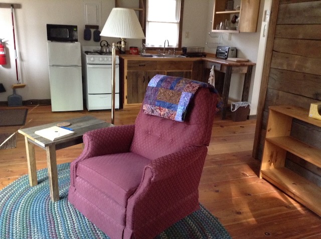 A red chair with a colorful quilt on top sits centered in the room of a small wood cabin.