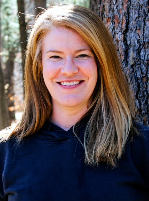 A woman with strawberry blond hair in a blue shirt smiles at the camera.