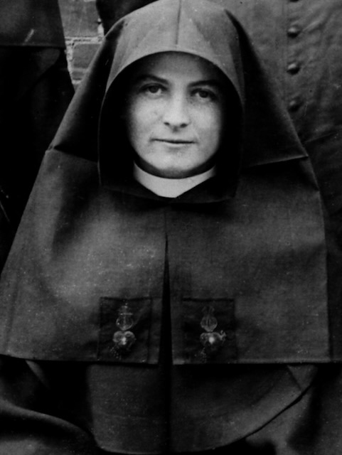 A black and white photo of a nun in habit looking at the camera with a stoic gaze.