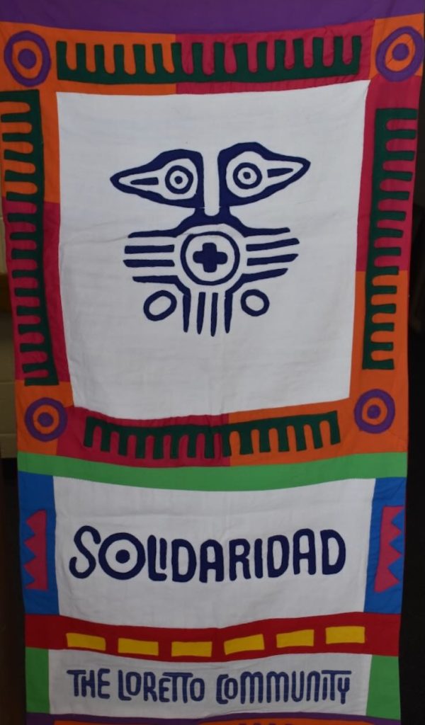 a colorful banner that features an indigenous symbol in the middle with the words "Solidaridad" and "The Loretto Community" underneath it.