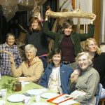 Seven women gather for a lighthearted photo at a dinner table in Jeanne Dueber's art studio.