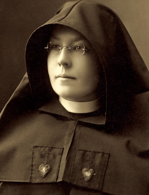 A sepia toned photo of a nun in habit with small round glasses looks to the right of the camera.