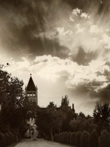 Sepia toned photo of a college building surrounded by trees. A Celtic cross graces the building's tower.