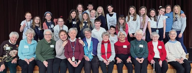 A large group picture of a wide variety of ages sitting and standing together for a group picture indoors. They are wearing name tags.