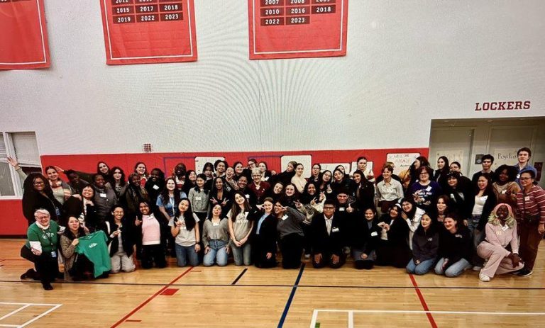 A large group of teenagers pose for a photo in a school gym.