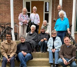Eleven smiling people pose for a photo on a set of stairs outside a red brick building.