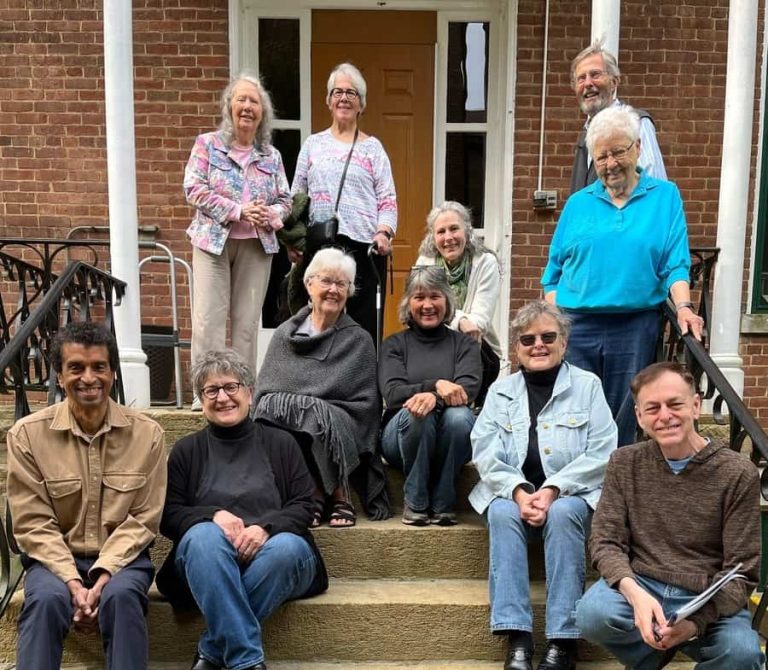 Eleven smiling people pose for a photo on a set of stairs outside a red brick building.