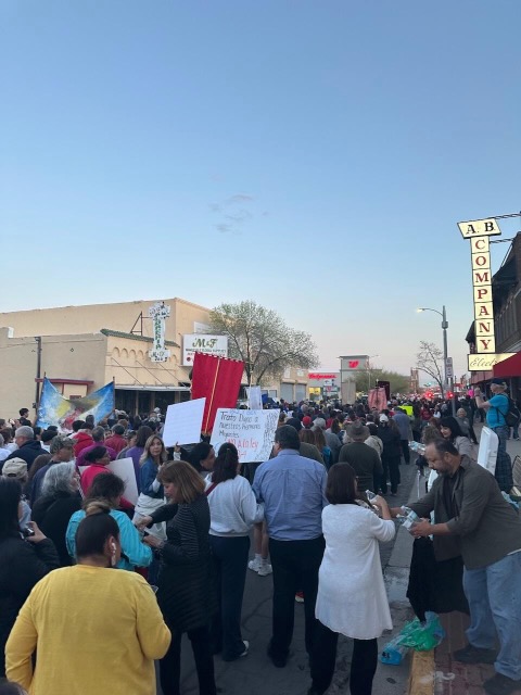 Photo of an ongoing protest showing the back of people's bodies marching with signs down an El Paso street.