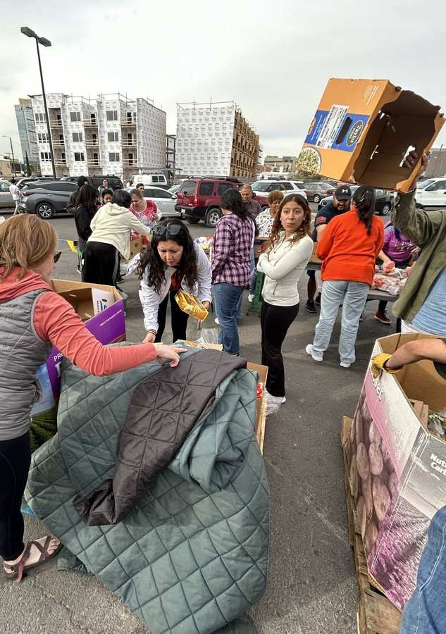Several people in a parking lot are shown looking through big boxes and sorting them for a charity.