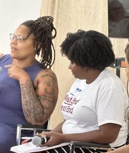 Two women conversing while sitting indoors at an event, one woman is holding a microphone.