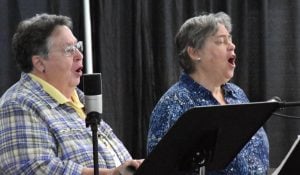 Two women sing their hearts out in front of microphones and music stands.