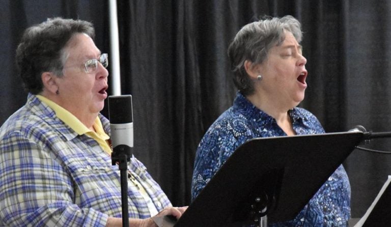 Two women sing their hearts out in front of microphones and music stands.
