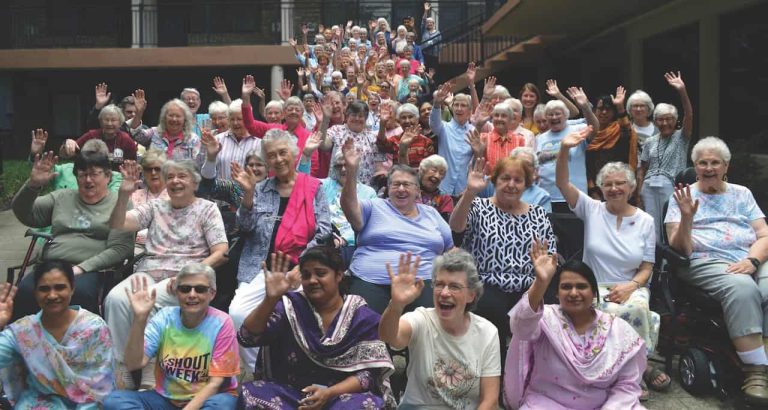 A group of about 100 women in a group drone picture giving an enthusiastic wave to the camera.