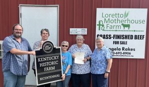 Five people stand in front of a red barn and smile together for a group picture while displaying an award plaque and paper certification that says Kentucky Historic Farm.