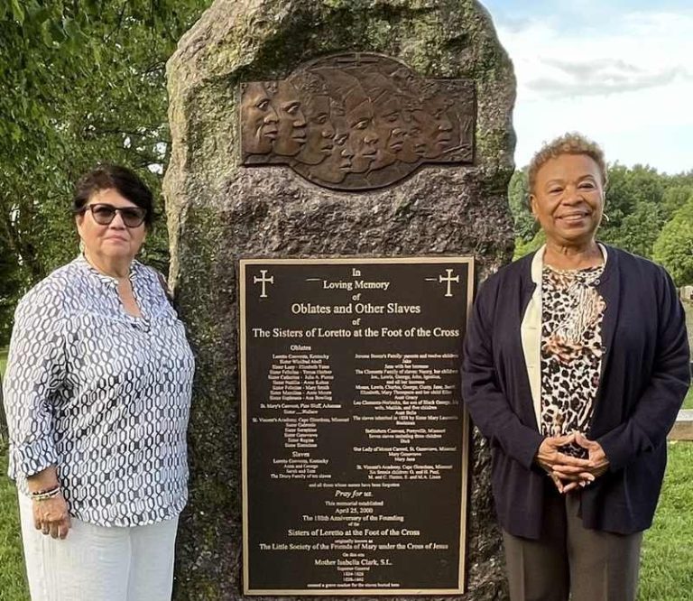 Two women standing and smiling together visiting a slave memorial site.