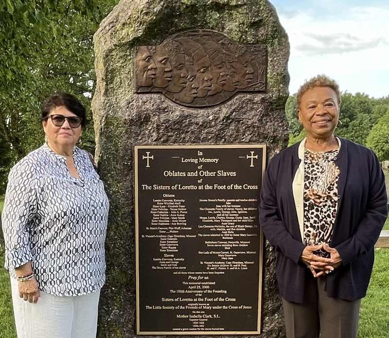 Two women standing and smiling together visiting a slave memorial site.