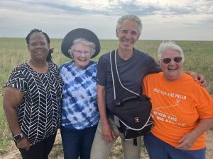 Four people - a Black woman, an older White woman, a middle-aged man and a second older White woman pose for a photo on the prairie.