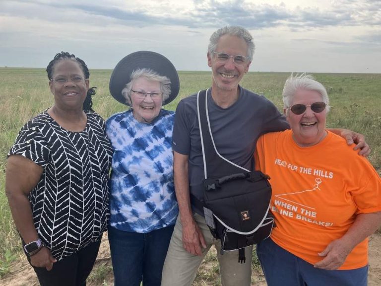 Four people - a Black woman, an older White woman, a middle-aged man and a second older White woman pose for a photo on the prairie.