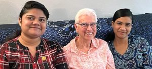 Three women sitting on a patterned couch in a room together smiling for a picture.