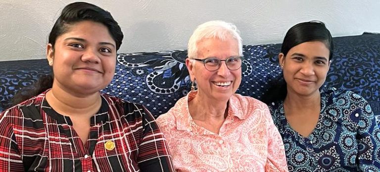 Three women sitting on a patterned couch in a room together smiling for a picture.