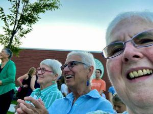 Three women enjoying a celebration among others outdoors on a sunny day.