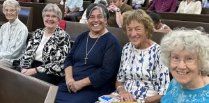 Five women smiling together while sitting in a row at church.