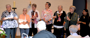 Seven women standing while holding candles on the front stage for an induction ceremony.