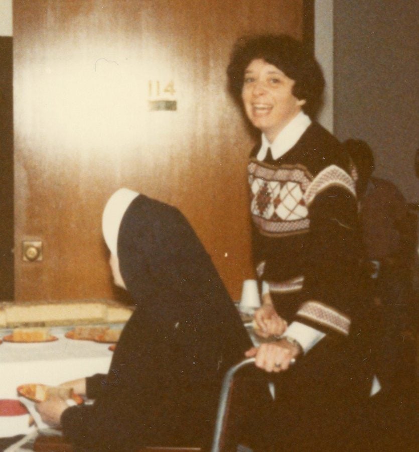 A woman with a beaming smile pushes a habited nun in a wheelchair.
