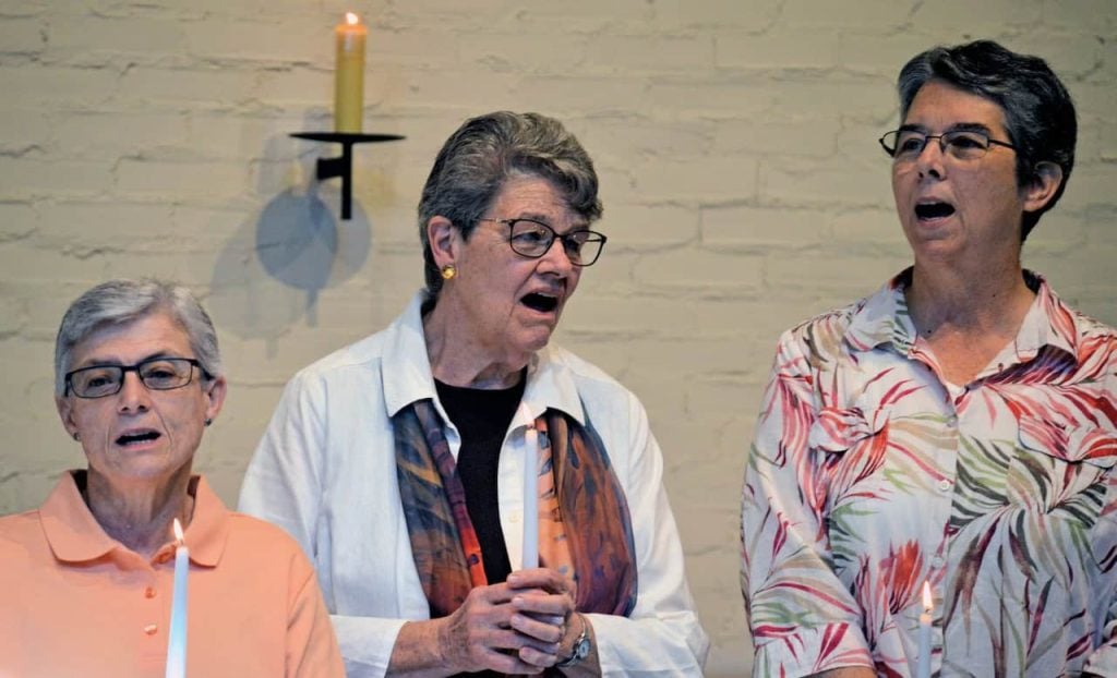 Three older women hold candles and sing