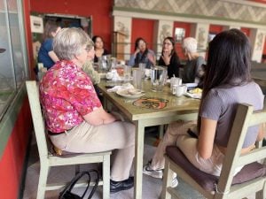 A group of people share a meal at a table together, listening to one person animatedly talk.