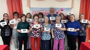 A large group of people, each holding a piece of paper with a number on it and many in nursing scrubs, pose for a photo.