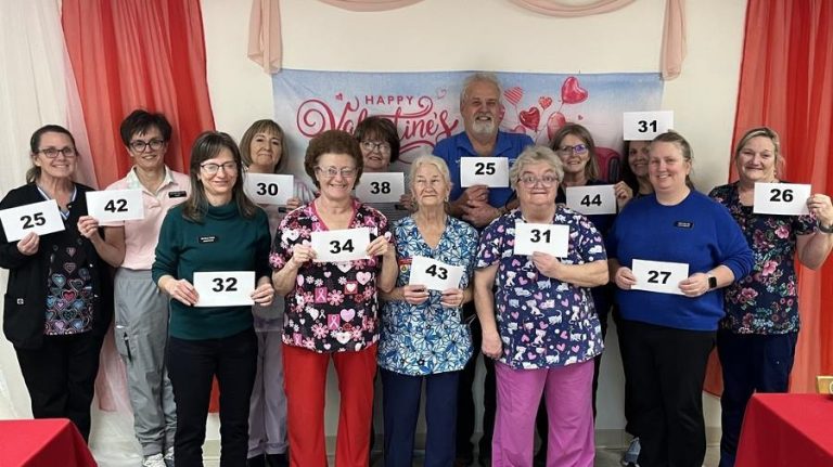 A large group of people, each holding a piece of paper with a number on it and many in nursing scrubs, pose for a photo.