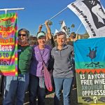 Older women protest outdoors carrying colorful banners